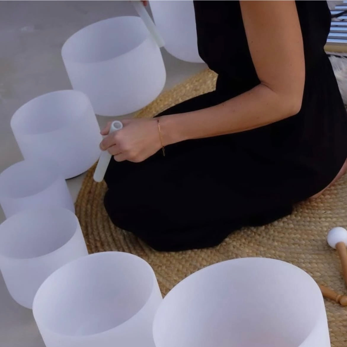 Person sitting on a woven mat with white singing bowls in front
